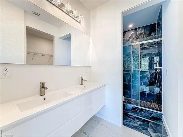Bathroom featuring double vanity, a marble finish shower, and light marble finish floors