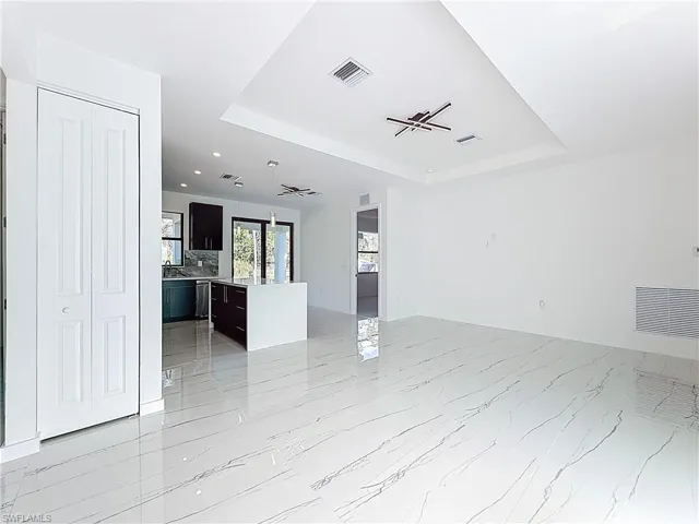 Unfurnished living room with a tray ceiling, recessed lighting, and light marble finish flooring