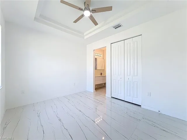 Unfurnished bedroom featuring a raised ceiling, a ceiling fan, a closet, and ensuite bath