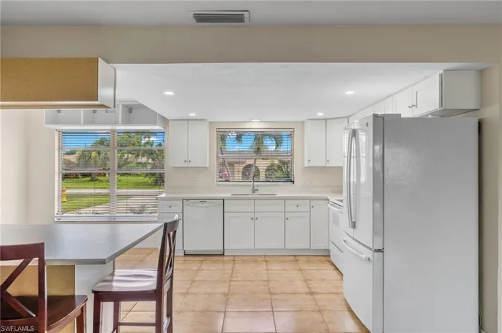 Kitchen featuring sink, white appliances, light tile patterned floors, and white cabinets