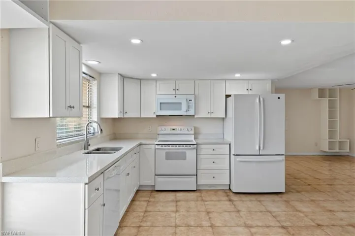 Kitchen with light tile patterned flooring, white cabinetry, white appliances, and sink
