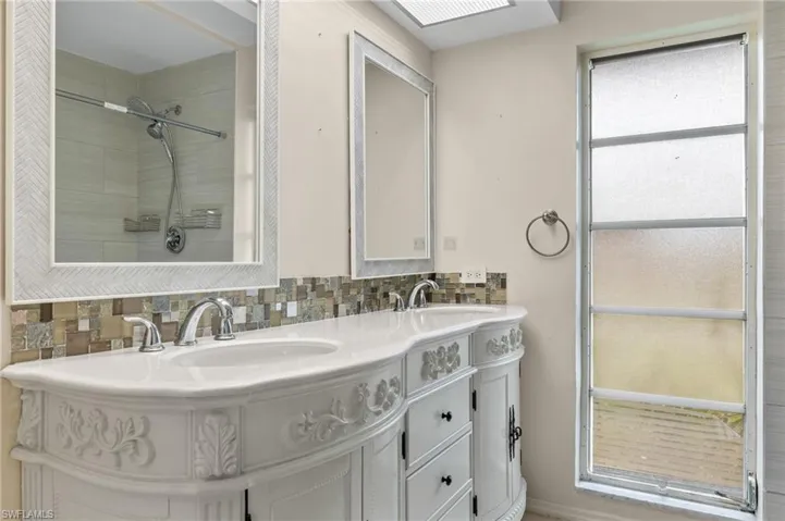Bathroom featuring walk in shower, a healthy amount of sunlight, tasteful backsplash, and dual bowl vanity