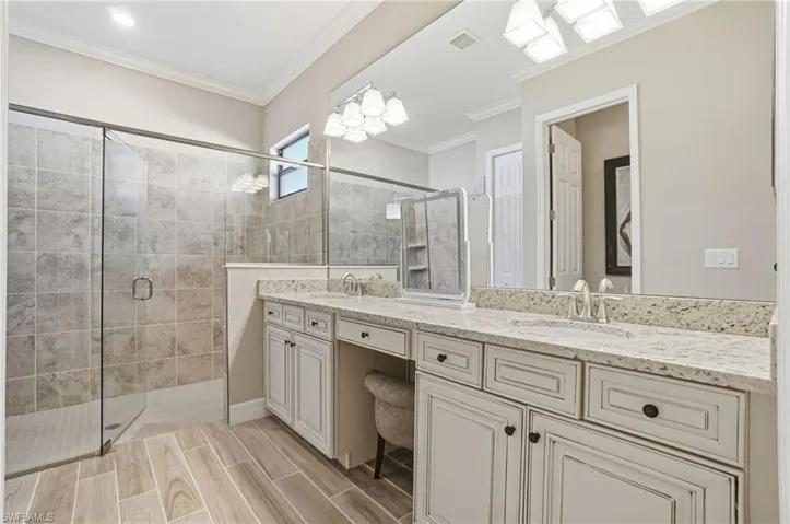 Bathroom featuring a stall shower, double vanity, ornamental molding, and wood tiled floors