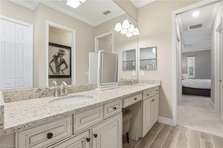 Ensuite bathroom featuring crown molding, double vanity, and a closet
