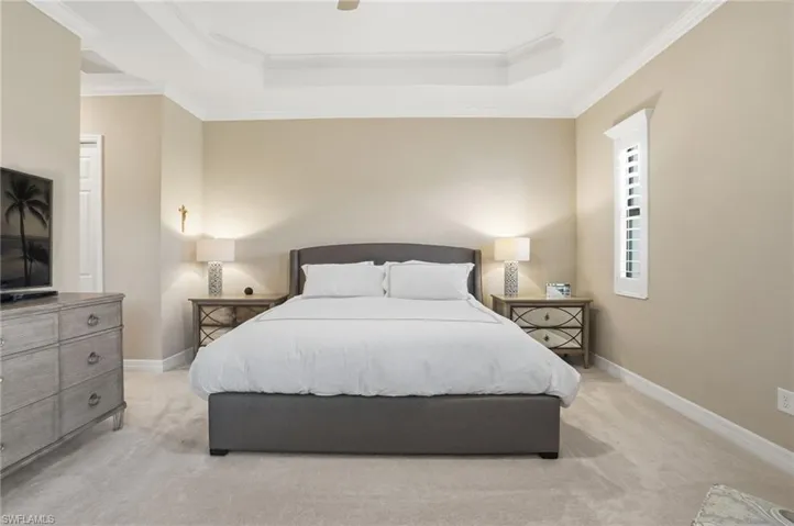 Carpeted bedroom with a tray ceiling, ceiling fan, and crown molding