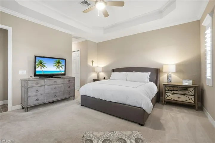 Bedroom with a closet, a raised ceiling, a ceiling fan, carpet, and crown molding