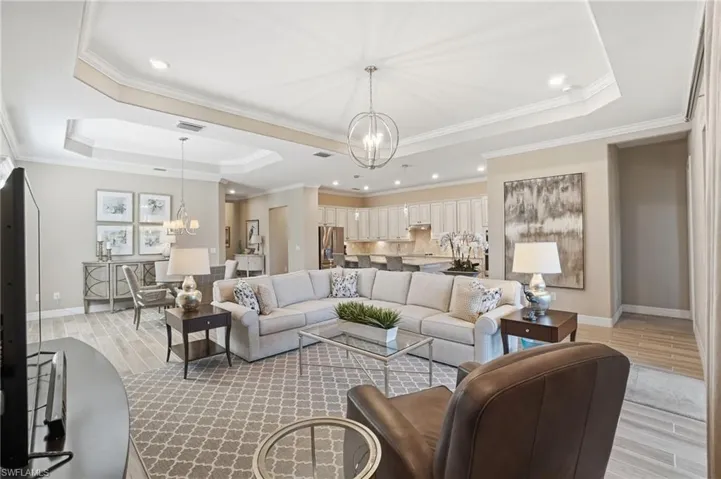 Living room with a tray ceiling, a chandelier, light wood finished floors, recessed lighting, and ornamental molding