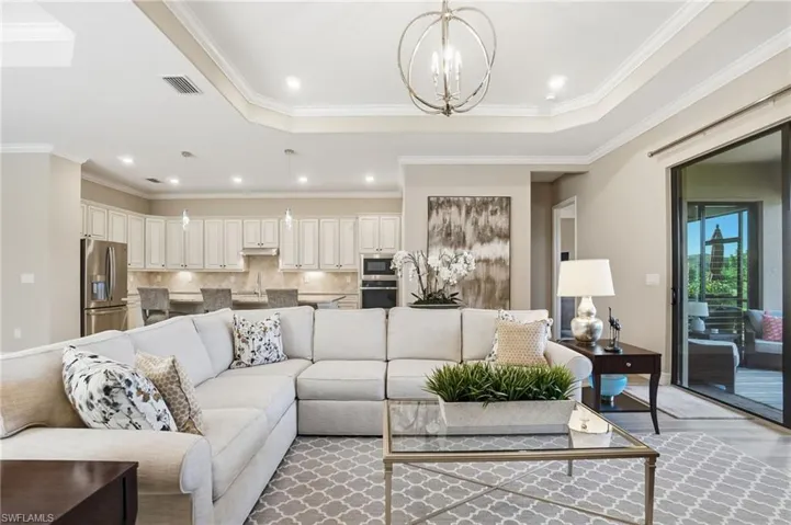Living area with a chandelier, recessed lighting, ornamental molding, a raised ceiling, and wood finished floors