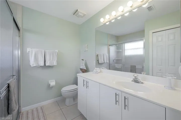 Bathroom featuring tile patterned floors, toilet, a shower with door, and vanity