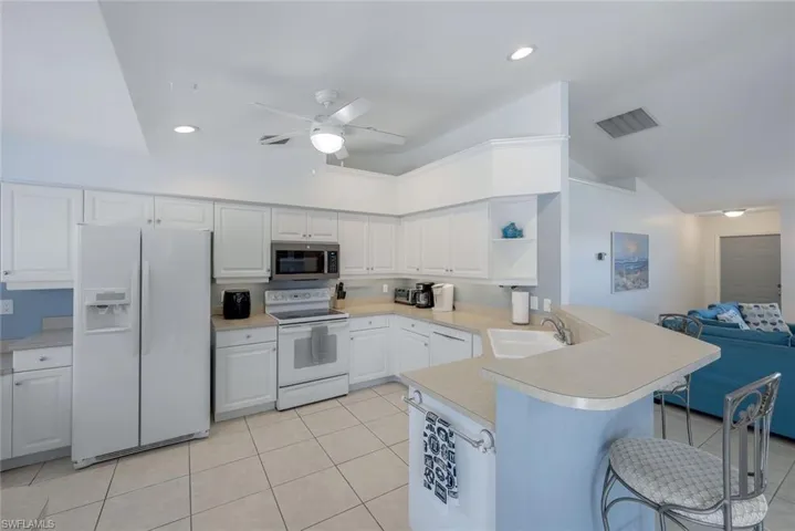 Kitchen with sink, light tile patterned floors, a kitchen breakfast bar, white appliances, and white cabinets
