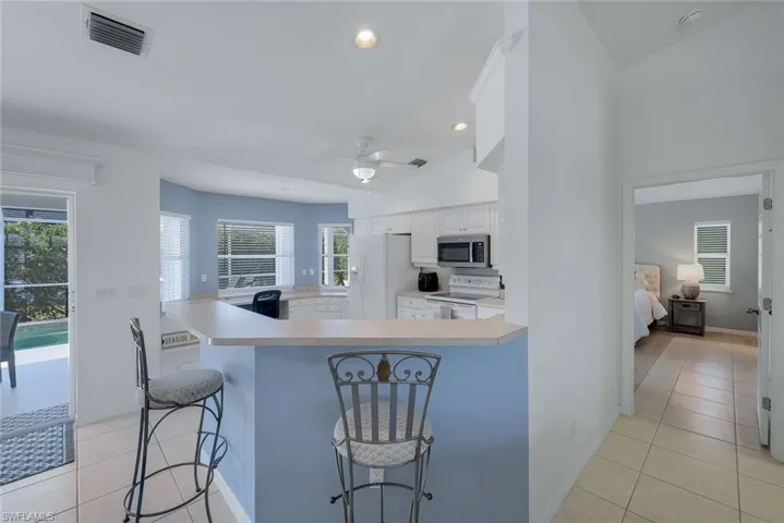 Kitchen featuring light tile patterned floors, white appliances, white cabinets, a kitchen bar, and kitchen peninsula