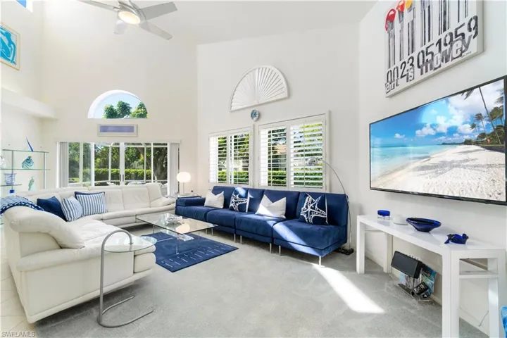 Carpeted living room featuring ceiling fan and a towering ceiling