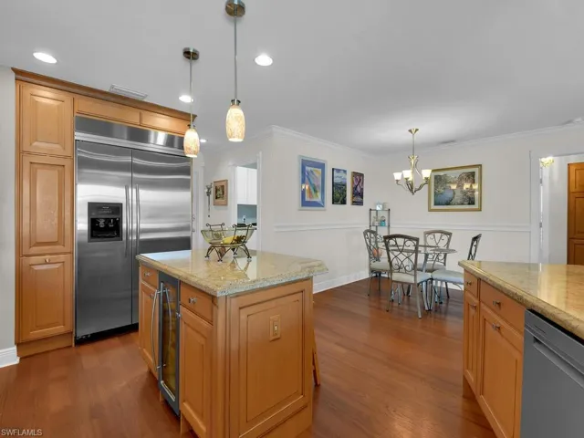 Kitchen with appliances with stainless steel finishes, dark wood-style flooring, beverage cooler, light stone counters, and ornamental molding