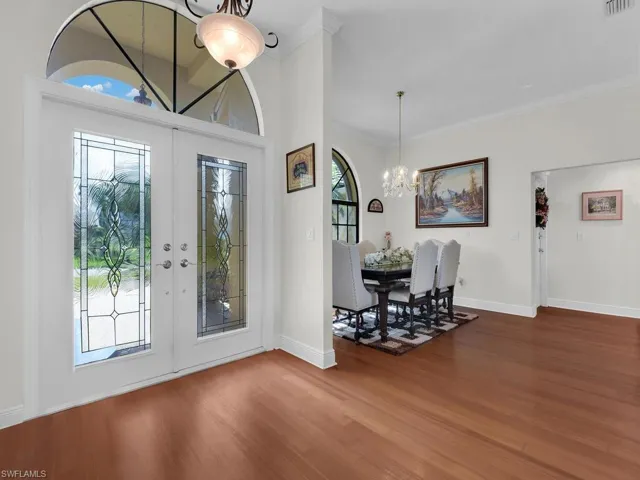 Foyer with a chandelier, french doors, wood finished floors, plenty of natural light, and ornamental molding