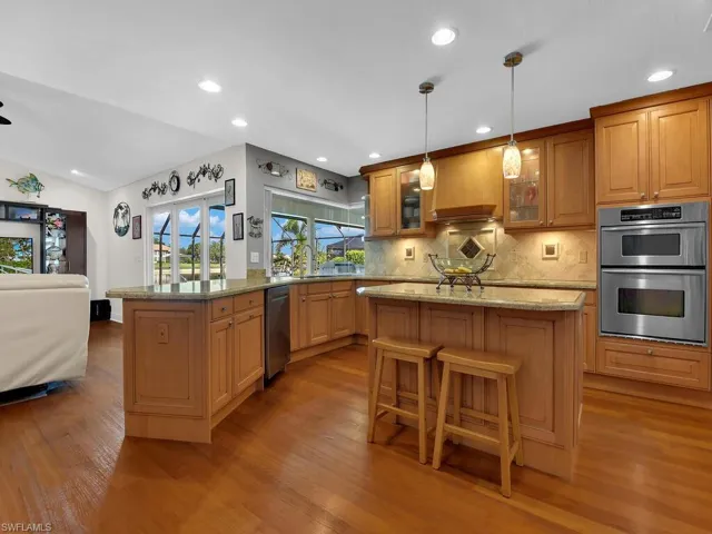 Kitchen with tasteful backsplash, appliances with stainless steel finishes, recessed lighting, light stone countertops, and glass insert cabinets