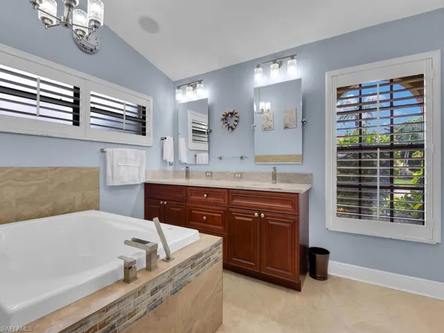 Full bath with double vanity, a garden tub, tile patterned floors, and a chandelier