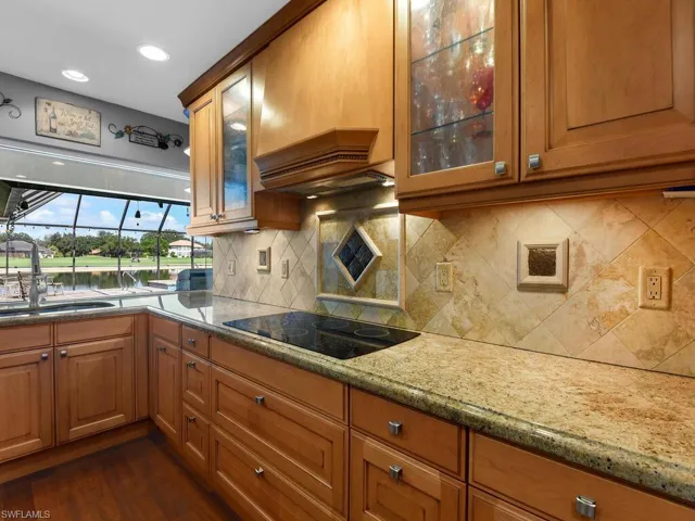 Kitchen featuring light stone countertops, brown cabinets, dark wood-style floors, glass insert cabinets, and recessed lighting