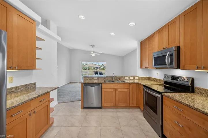 Kitchen with stainless steel appliances, light stone counters, a peninsula, vaulted ceiling, and wood finish cabinets