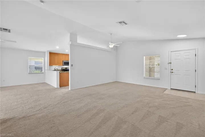 Unfurnished living room with ceiling fan, vaulted ceiling, recessed lighting, light colored carpet, and healthy amount of natural light