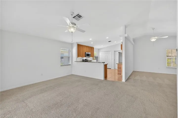 Unfurnished living room featuring ceiling fan, light colored carpet, lofted ceiling, and recessed lighting