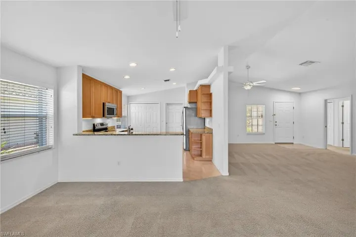 Kitchen with wood finish cabinetry, a ceiling fan, light carpet, a peninsula, and dark stone countertops