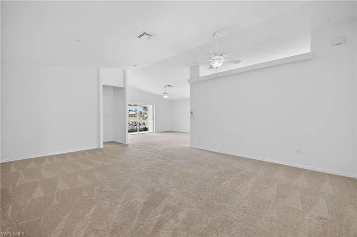 Empty room featuring light colored carpet, vaulted ceiling, and ceiling fan