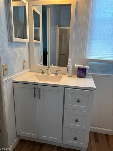 Full bathroom featuring a wainscoted wall, wallpapered walls, vanity, dark wood-style floors, and a shower stall