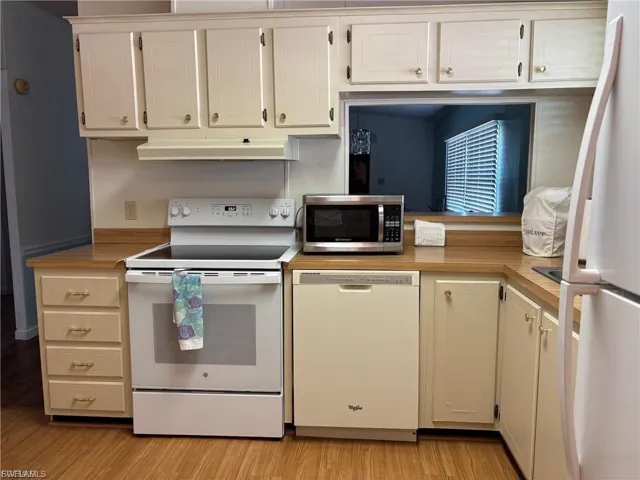 Kitchen with white appliances, light countertops, light wood-type flooring, and under cabinet range hood