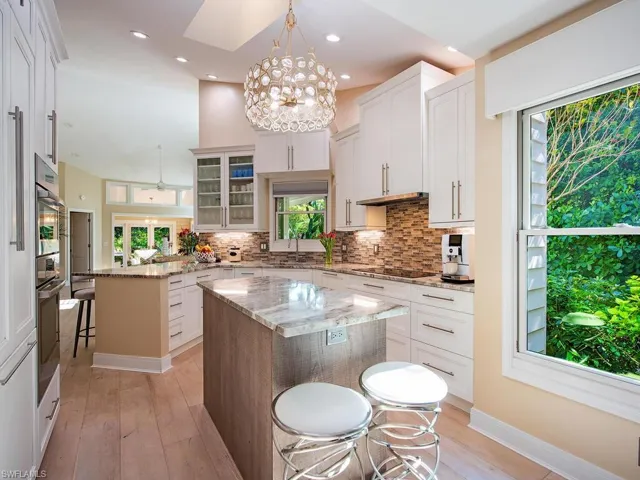 Kitchen featuring a breakfast bar, glass insert cabinets, light stone countertops, a center island, and peninsula