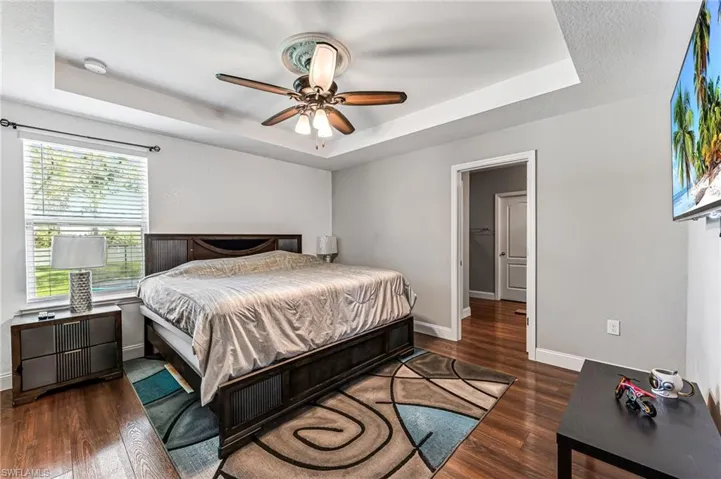 Bedroom with dark hardwood / wood-style floors, ceiling fan, and a raised ceiling