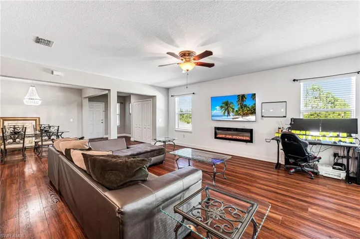 Living room with a textured ceiling, ceiling fan, and dark hardwood / wood-style floors