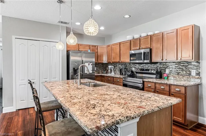 Kitchen with dark hardwood / wood-style floors, an island with sink, stainless steel appliances, hanging light fixtures, and sink