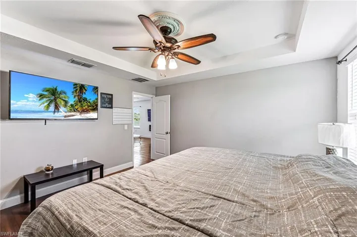 Bedroom with multiple windows, a tray ceiling, ceiling fan, and dark hardwood / wood-style flooring