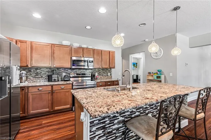 Kitchen with dark hardwood / wood-style flooring, backsplash, hanging light fixtures, a breakfast bar area, and appliances with stainless steel finishes