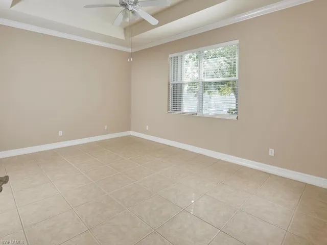 Tiled empty room with ceiling fan, ornamental molding, and a tray ceiling