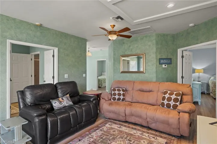 Living room with wood finished floors, a ceiling fan, and wallpapered walls