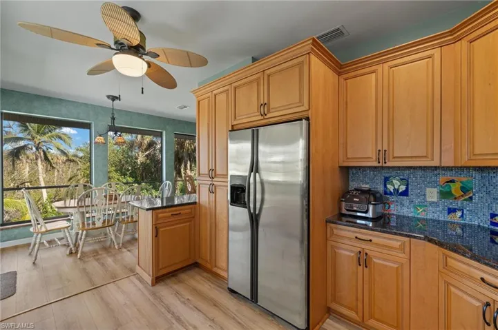 Kitchen featuring stainless steel refrigerator with ice dispenser, light wood finished floors, tasteful backsplash, dark stone counters, and hanging light fixtures