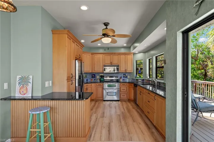 Kitchen featuring light wood finished floors, appliances with stainless steel finishes, tasteful backsplash, dark stone countertops, and recessed lighting