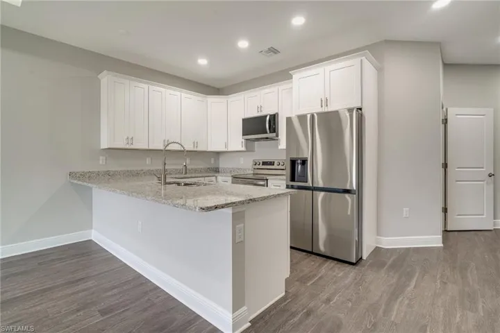 Kitchen featuring stainless steel appliances, white cabinets, light stone counters, dark wood-style flooring, and a peninsula