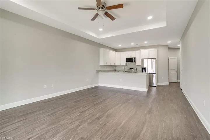 Unfurnished living room with recessed lighting, a ceiling fan, dark wood-type flooring, and a tray ceiling