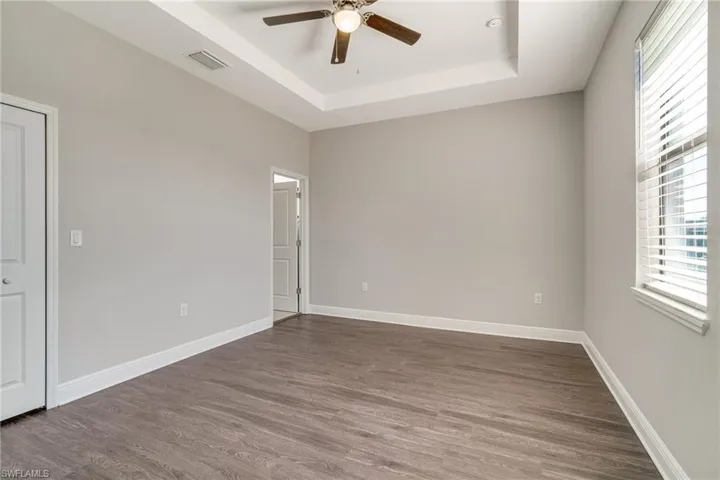 Unfurnished room featuring a tray ceiling, ceiling fan, and wood finished floors