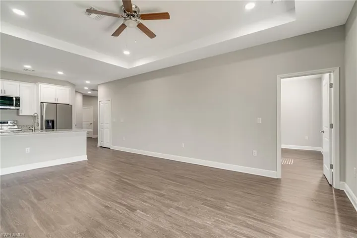 Unfurnished living room featuring recessed lighting, ceiling fan, a raised ceiling, and dark wood-style flooring