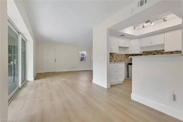 Kitchen with white cabinetry, decorative backsplash, light wood-style flooring, under cabinet range hood, and open floor plan