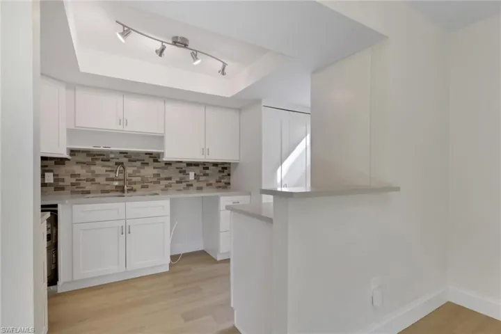 Kitchen featuring white cabinets, decorative backsplash, light wood-style floors, and a tray ceiling
