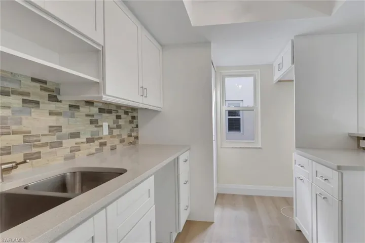 Kitchen with white cabinetry, decorative backsplash, open shelves, light wood-style floors, and light stone countertops