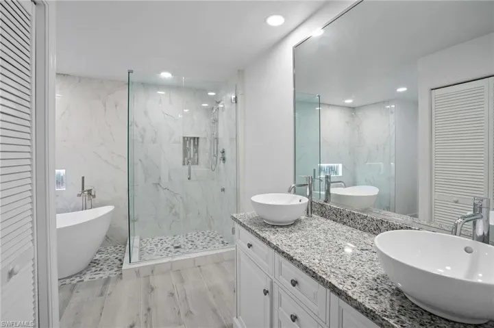 Bathroom featuring a closet, double vanity, a freestanding tub, a marble finish shower, and recessed lighting