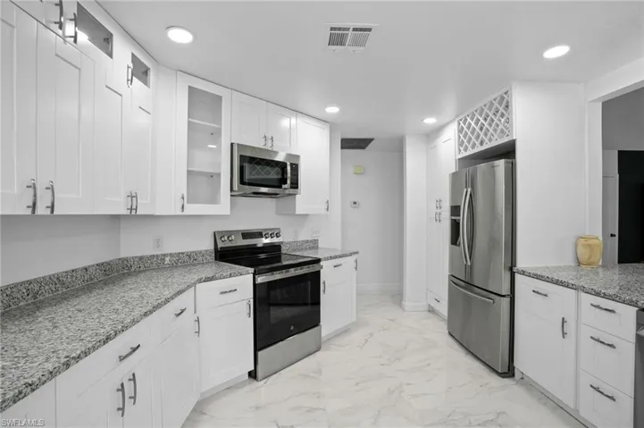 Kitchen with glass insert cabinets, appliances with stainless steel finishes, light stone counters, and recessed lighting