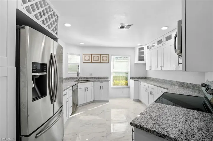 Kitchen with light stone counters, stainless steel appliances, glass insert cabinets, white cabinetry, and recessed lighting