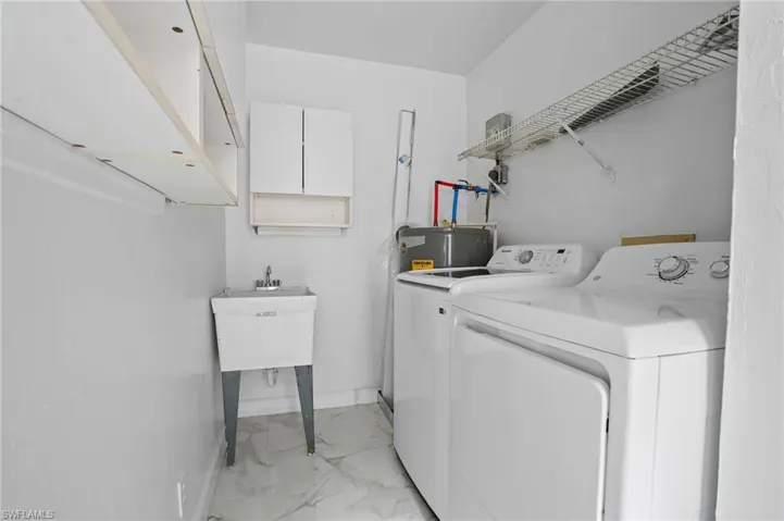Laundry room with light marble finish floors, cabinet space, washing machine and dryer, and electric water heater