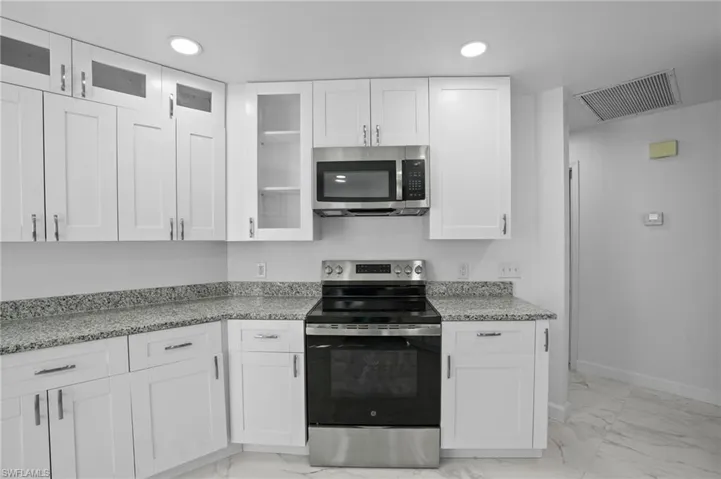 Kitchen featuring appliances with stainless steel finishes, white cabinetry, light stone countertops, glass insert cabinets, and light marble finish floors